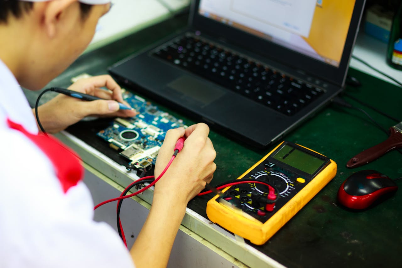 Technician working on a laptop with multimeter in a professional workspace.